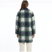 A woman viewed from the back wearing a green, navy, and off-white plaid coat over cream pants, set against a plain white background.