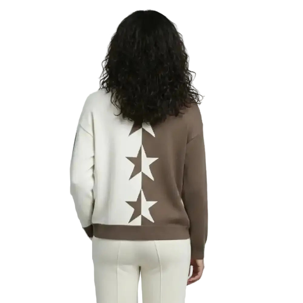 A woman viewed from behind wearing a color-blocked knit sweater with a large vertical star pattern on the back, paired with white pants, against a plain light gray studio background.