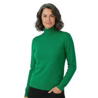 A woman wearing a bright green ribbed turtleneck sweater, paired with black pants, standing against a plain white studio background.