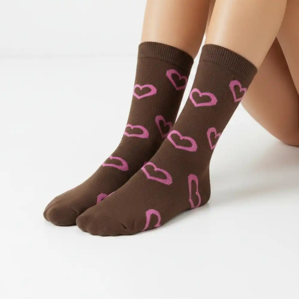 A pair of brown crew socks with a pink heart pattern, shown on a model's feet against a clean white background.