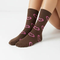 A pair of brown crew socks with a pink heart pattern, shown on a model's feet against a clean white background.