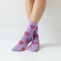 A pair of light purple ankle socks with red heart outlines, worn on a person's feet against a clean white background.