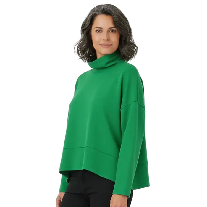 A woman wearing a bright green long-sleeve turtleneck sweater with a relaxed, cropped fit, paired with black pants, against a plain white studio background.