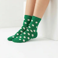 A pair of green ankle socks with white polka dots worn on a person's feet, shown against a clean white background.