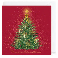 A square Christmas greeting card with a red background, featuring an illustrated green Christmas tree with gold lights, ornaments, a gold star topper, and the words 'Merry Christmas' at the bottom. A white envelope is partially visible behind the card.