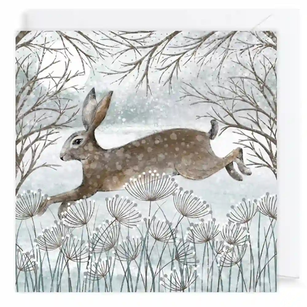A square art print or card featuring a watercolor-style winter scene with a brown hare jumping across pale blue-gray grasses beneath bare tree branches.