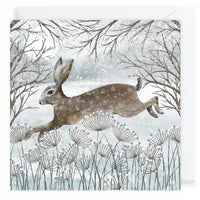 A square art print or card featuring a watercolor-style winter scene with a brown hare jumping across pale blue-gray grasses beneath bare tree branches.