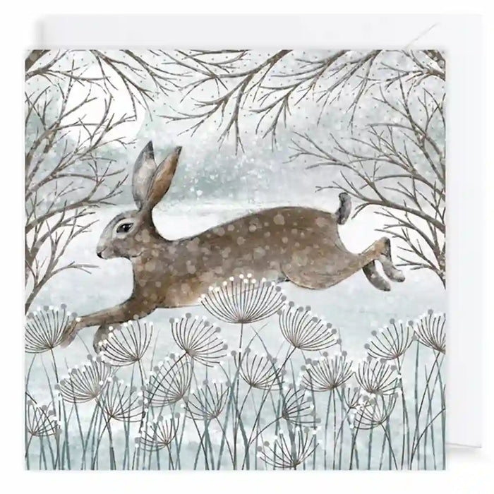 A square art print or card featuring a watercolor-style winter scene with a brown hare jumping across pale blue-gray grasses beneath bare tree branches.
