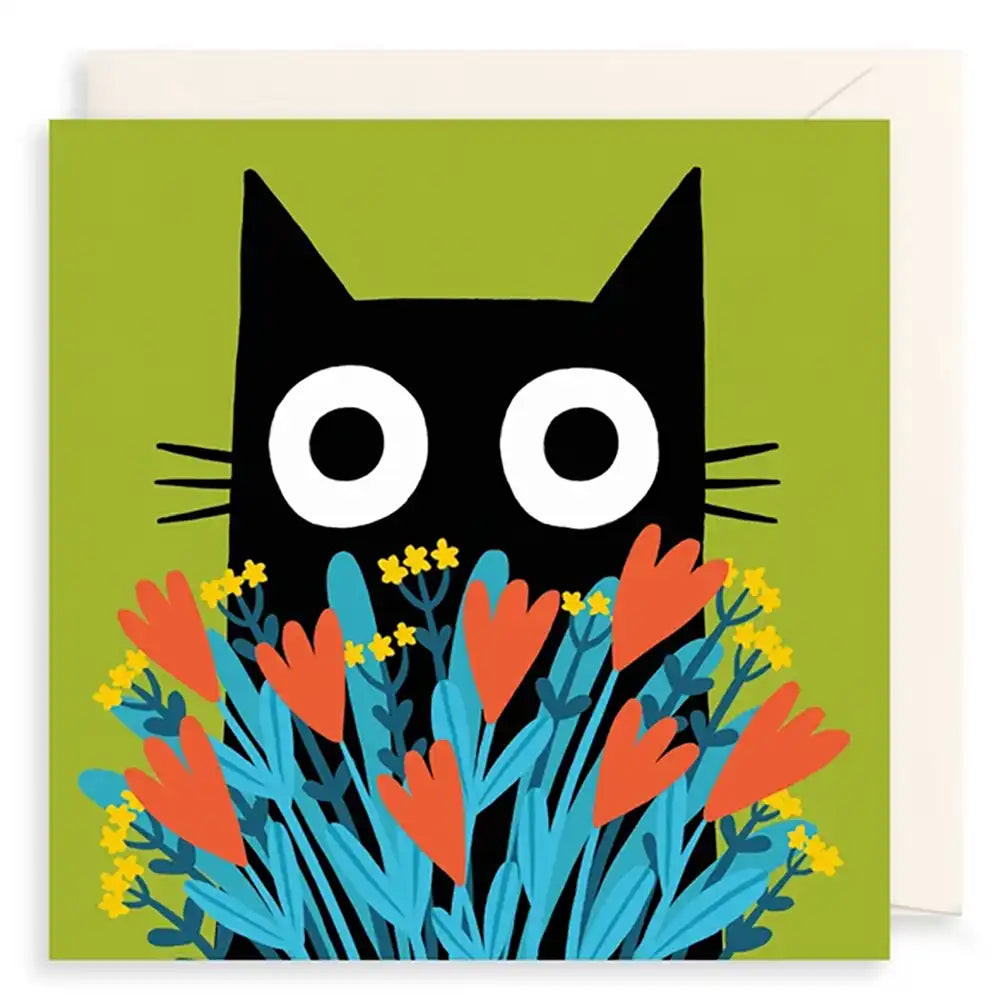 A square greeting card featuring a stylized black cat face with large white eyes peeking above a cluster of blue, orange, and yellow flowers on an olive green background. A white envelope is partially visible behind the card.