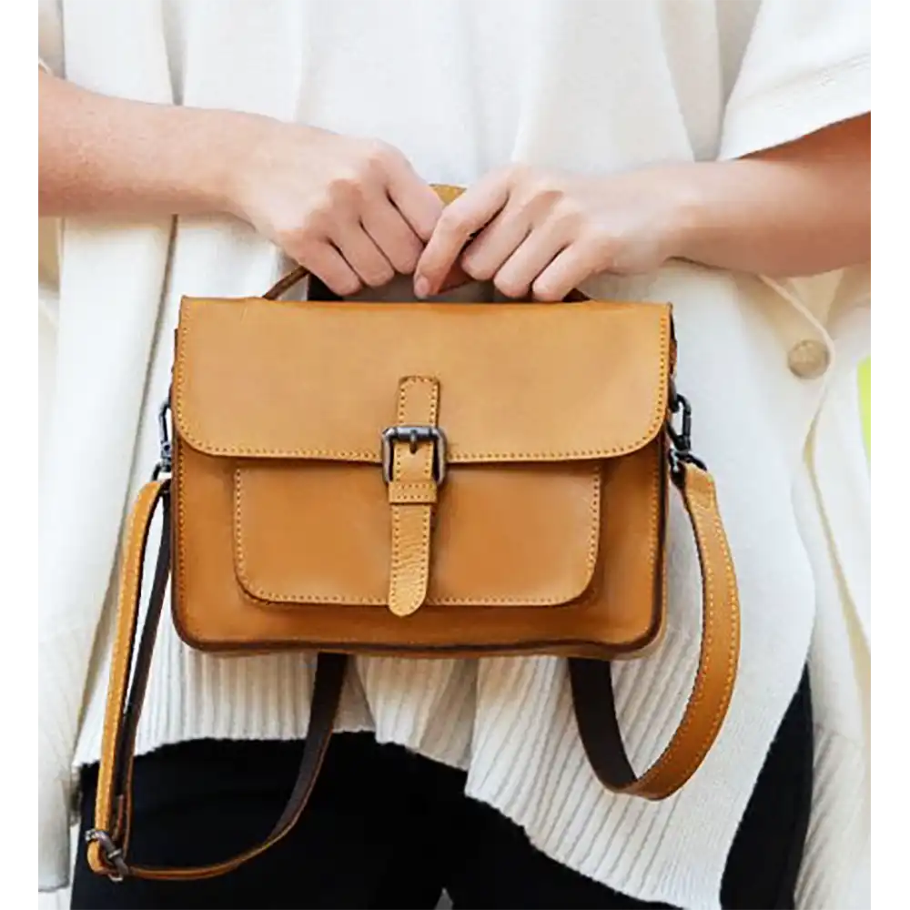 Brown leather handbag held by a person wearing a white sweater.