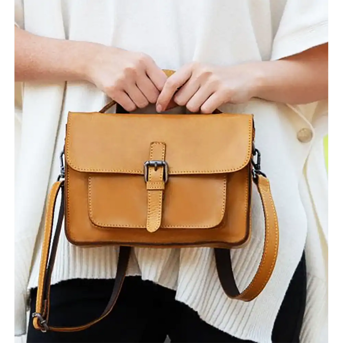 Brown leather handbag held by a person wearing a white sweater.