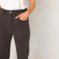 A person wearing dark charcoal gray slim-fit jeans with a white top, standing against a light gray background.