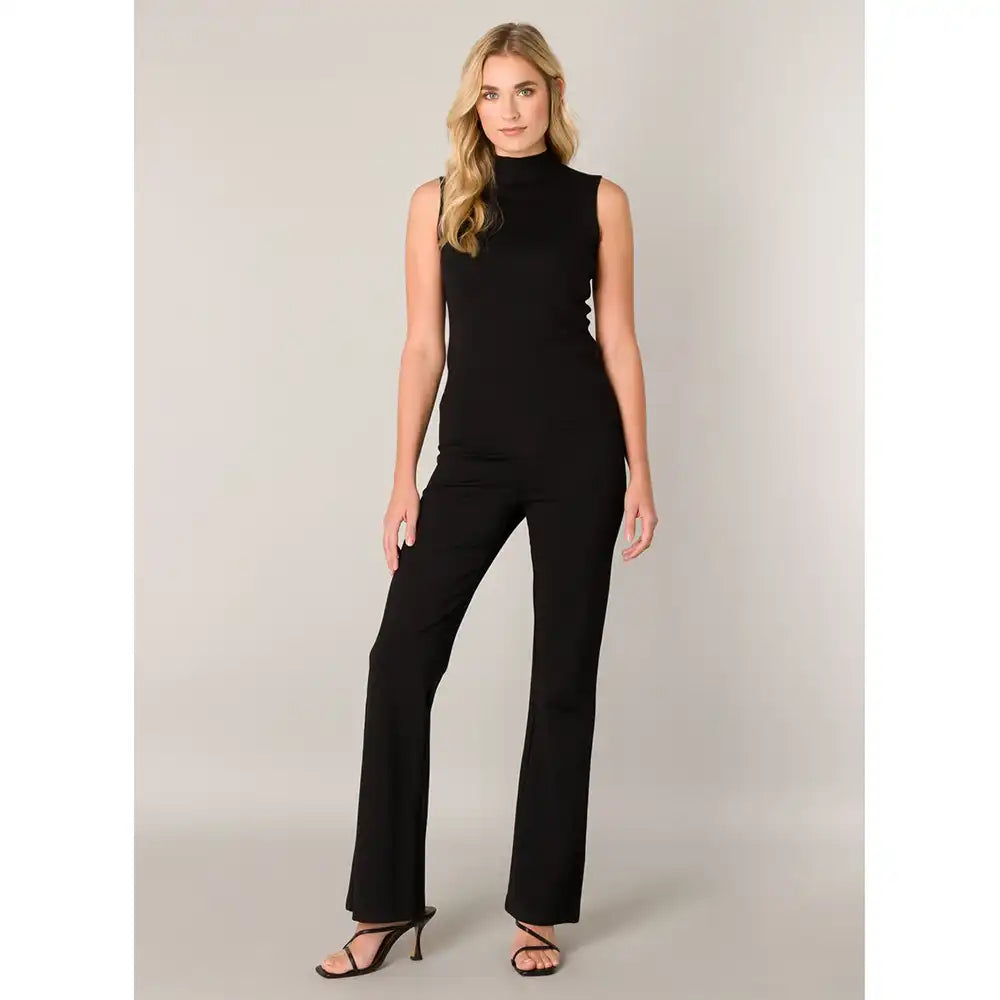 A woman modeling wide-leg blacj pants, paired with black strappy high-heeled sandals, against a neutral light gray studio background.