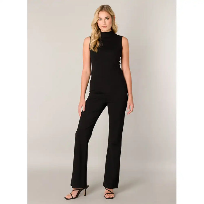 A woman modeling wide-leg blacj pants, paired with black strappy high-heeled sandals, against a neutral light gray studio background.