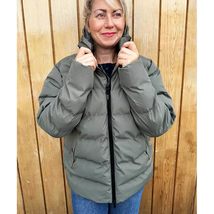 Woman wearing a gray puffer jacket against a wooden background
