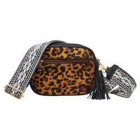 A leopard print crossbody bag with a wide, patterned woven strap, gold-tone hardware, and a black tassel, shown on a plain white background.