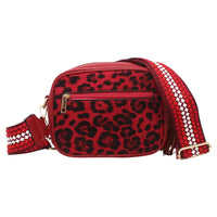 A red and black leopard print crossbody bag with a woven red, white, and black strap, featuring gold-tone hardware on a plain white background.