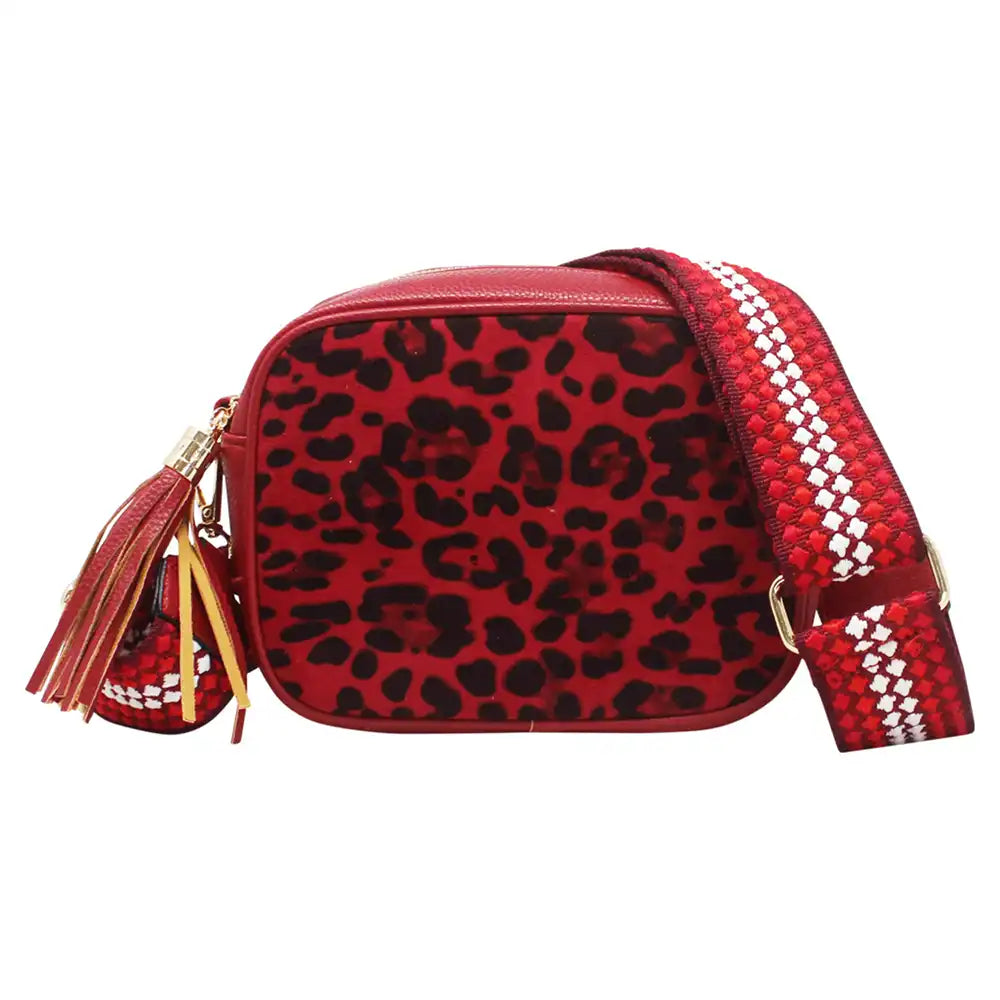 A red and black leopard print crossbody bag with a woven red and white strap, gold-tone hardware, and a matching tassel charm, shown against a plain white background.