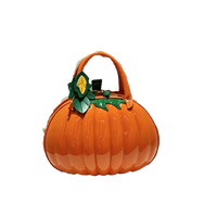 An orange pumpkin-shaped handbag with a glossy finish, featuring a top handle and a green leafy stem detail on the front, set against a plain white background.