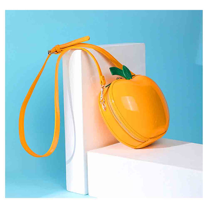 A glossy orange-shaped crossbody bag with a matching wrist strap, styled on white display blocks against a light blue background.