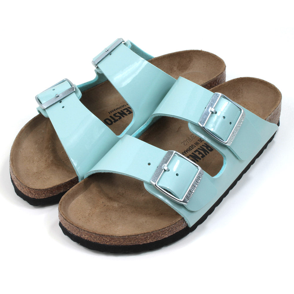 Birkenstock cork and rubber soled, two strap sandals. Two silver buckles on two patent surf green wide straps. Backless design with sculpted insole. Angled view.