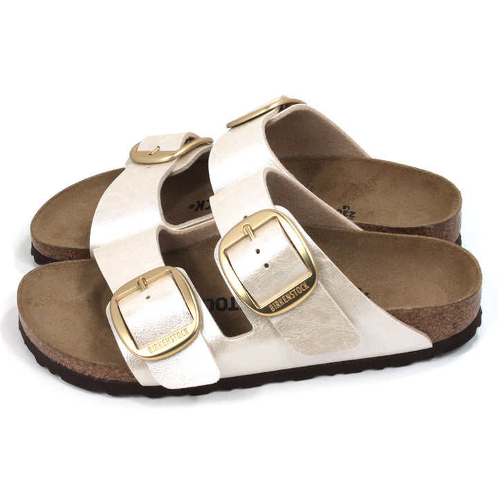 Birkenstock off white metallic two strap open back sandals. Large gold buckles. Cork inner soles and black rubber soles. Side view.