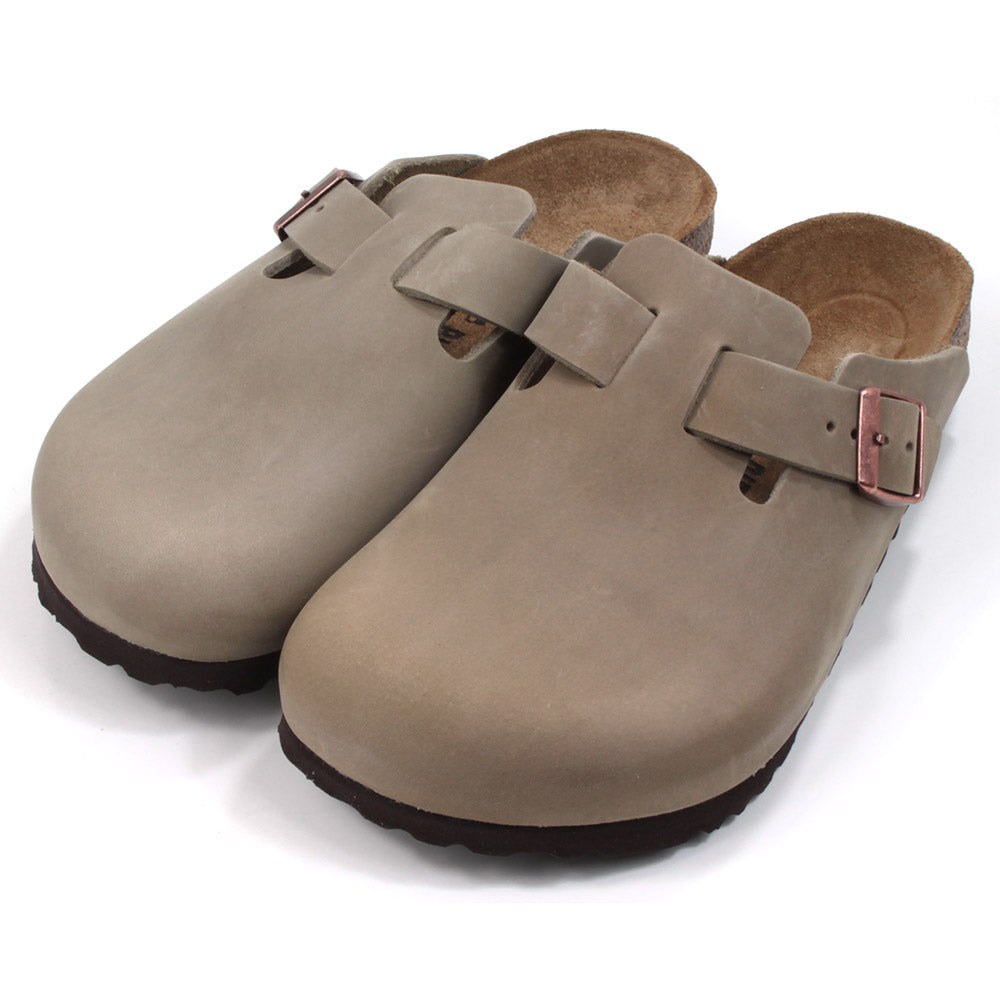 Birkenstock enclosed feet, open back clogs. Brown sculpted inner sole. Black rubber soles. Mid brown with copper coloured buckle on cross foot adjustment strap. Angled view.