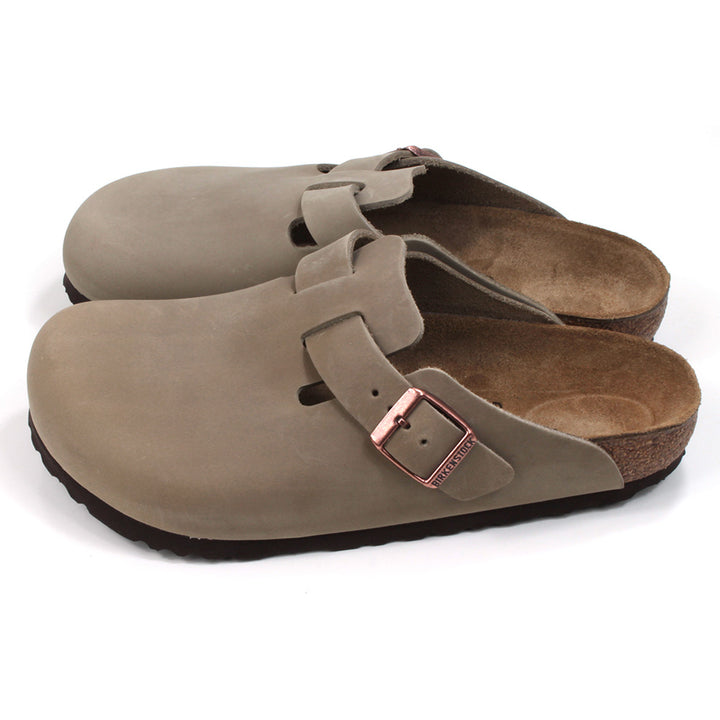 Birkenstock enclosed feet, open back clogs. Brown sculpted inner sole. Black rubber soles. Mid brown with copper coloured buckle on cross foot adjustment strap. Side view.