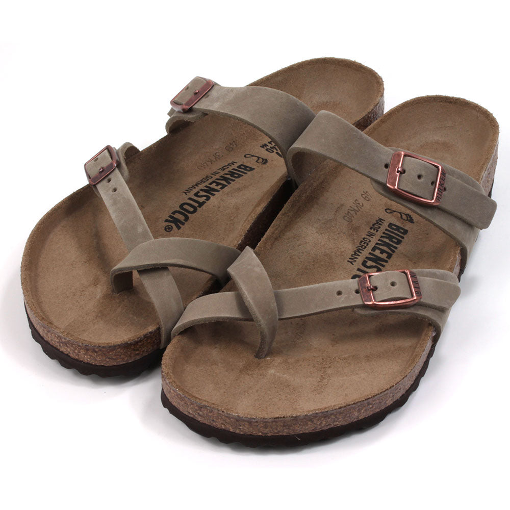 Birkenstock Mayari strapped sandals with open back design. Sculpted inner sole. Sole made of cork and black rubber. Straps over the big toe form a toe post design with another strap across the foot near the ankle. Adjustment with copper coloured buckles. Straps are a mid brown colour. Angled view.