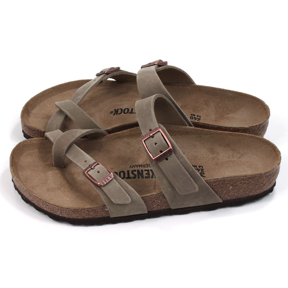 Birkenstock Mayari strapped sandals with open back design. Sculpted inner sole. Sole made of cork and black rubber. Straps over the big toe form a toe post design with another strap across the foot near the ankle. Adjustment with copper coloured buckles. Straps are a mid brown colour. Side view.