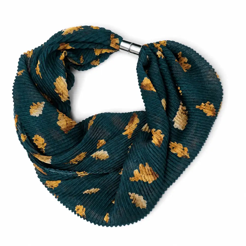 A pleated infinity scarf in dark teal green with a pattern of mustard yellow and cream leaves, secured with a silver metal clasp, shown on a plain white background.