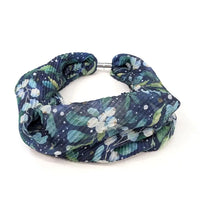 A crinkled fabric headband with a navy blue background, decorated with a green and white floral pattern, and secured with a silver metal clasp, shown on a plain white background.