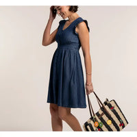 Woman wearing a blue dress holding a straw bag against a plain background