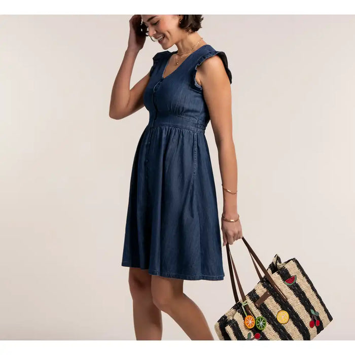Woman wearing a blue dress holding a straw bag against a plain background