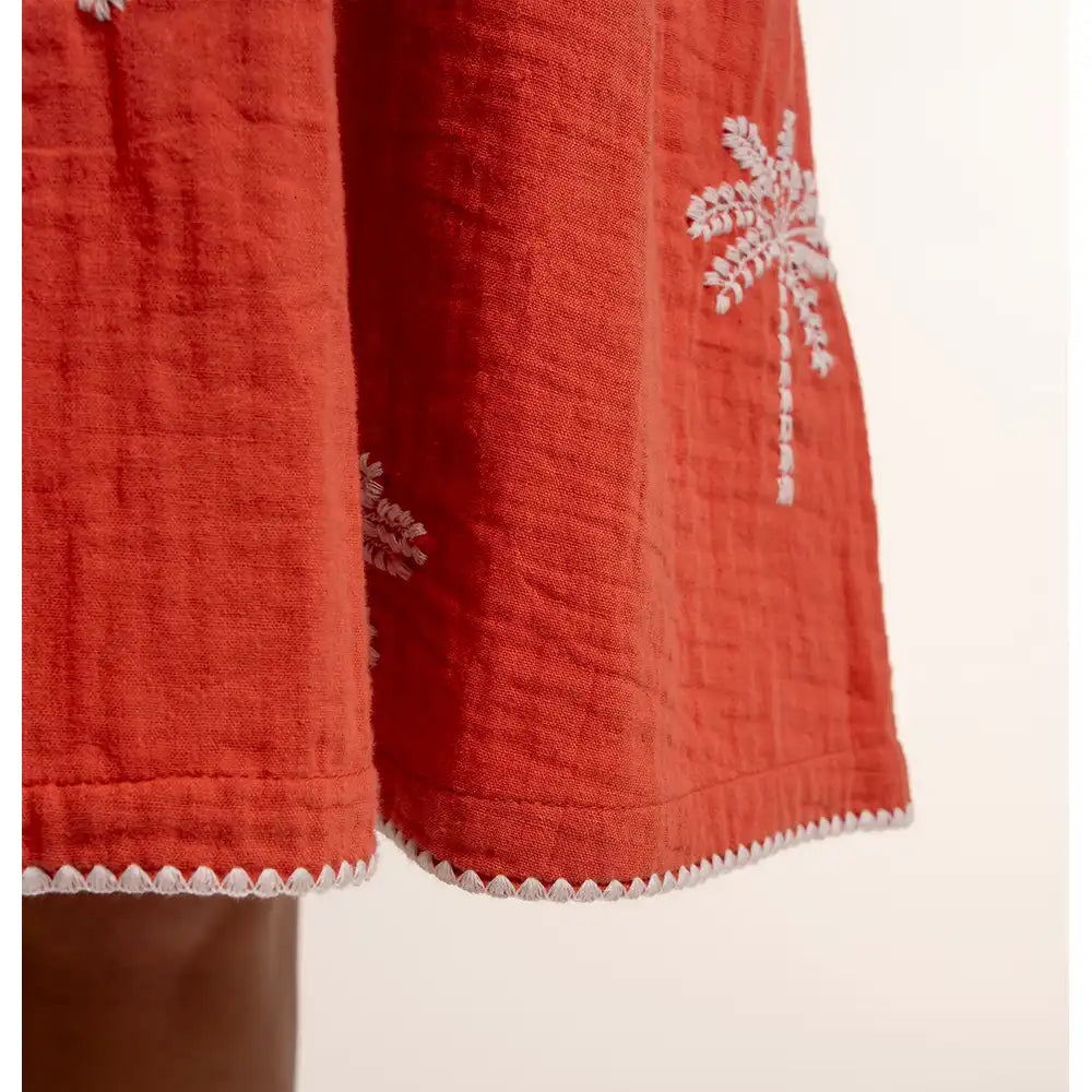 Red fabric with white floral embroidery on a beige background