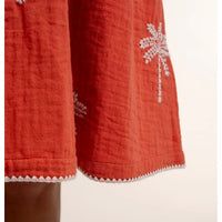 Red fabric with white floral embroidery on a beige background