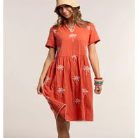 Woman wearing an orange dress with palm tree patterns on a beige background