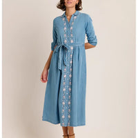 Woman wearing a blue denim dress with floral embroidery on a beige background