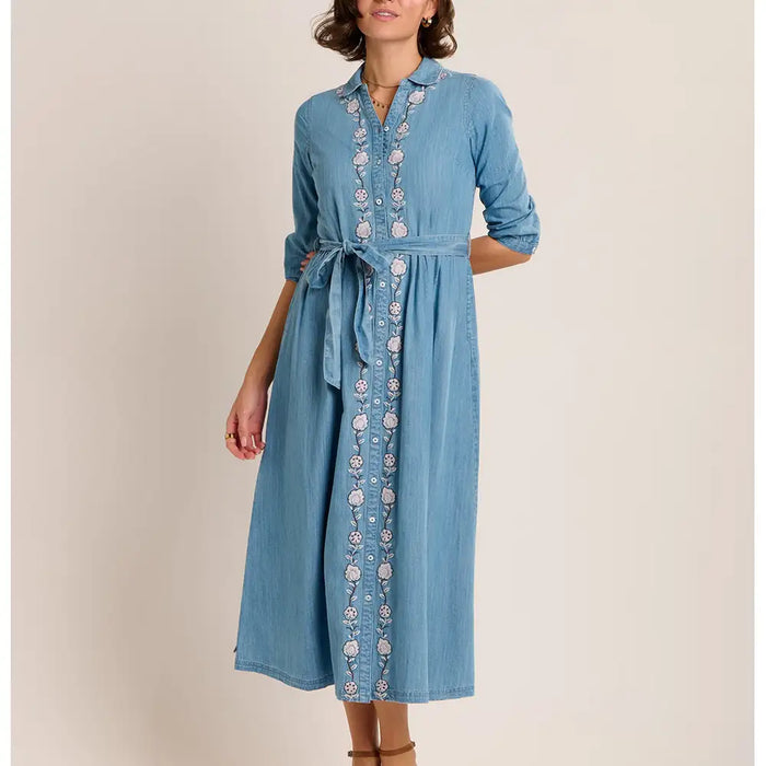 Woman wearing a blue denim dress with floral embroidery on a beige background