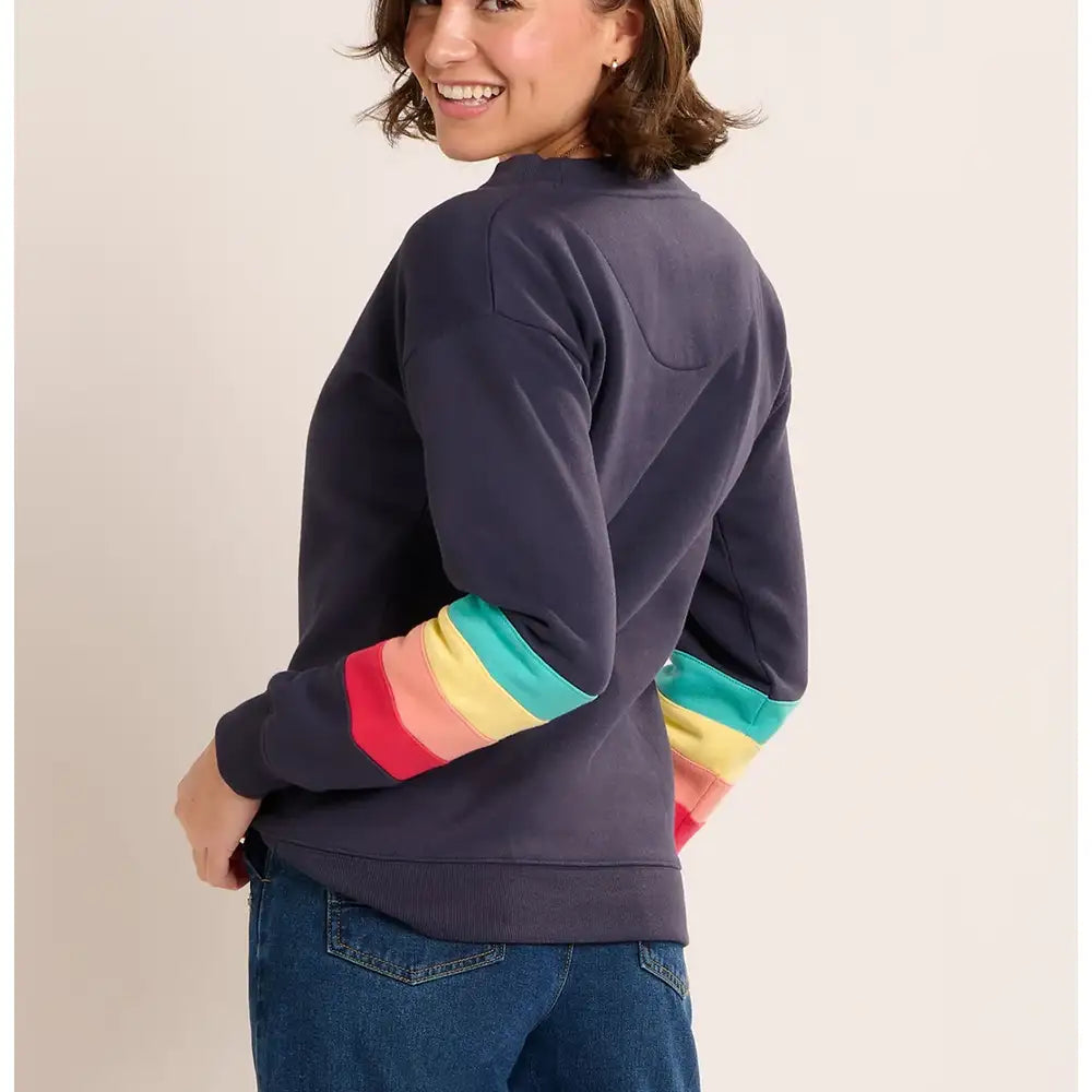 Person wearing a navy sweatshirt with rainbow sleeves on a beige background