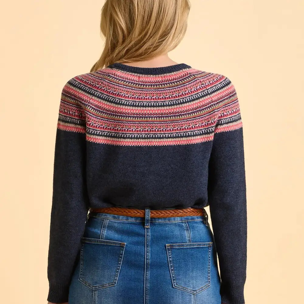 Person wearing a navy sweater with colorful pattern and blue jeans on a beige background
