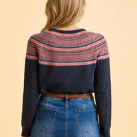 Person wearing a navy sweater with colorful pattern and blue jeans on a beige background