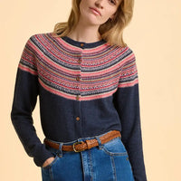 Woman wearing a navy sweater with colorful pattern and blue jeans on a beige background
