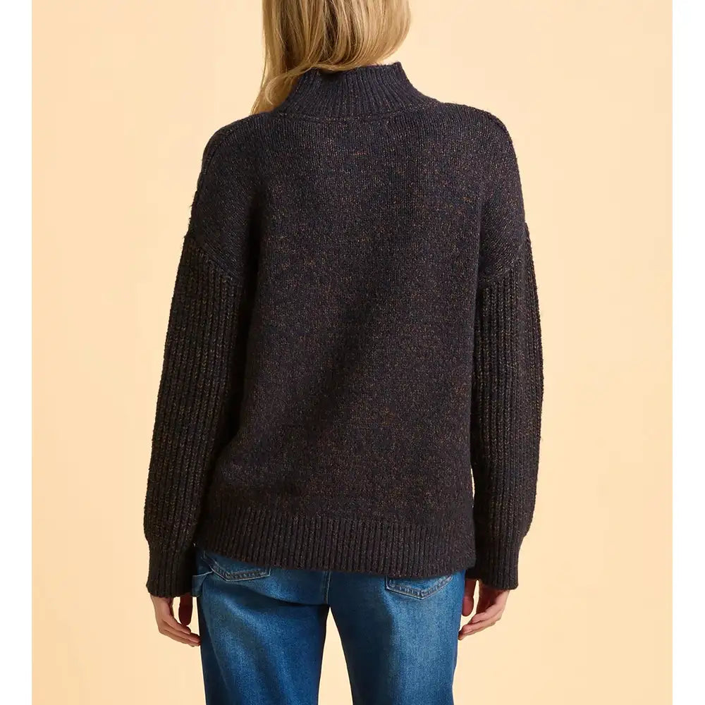 Person wearing a dark sweater and blue jeans on a beige background