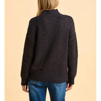 Person wearing a dark sweater and blue jeans on a beige background