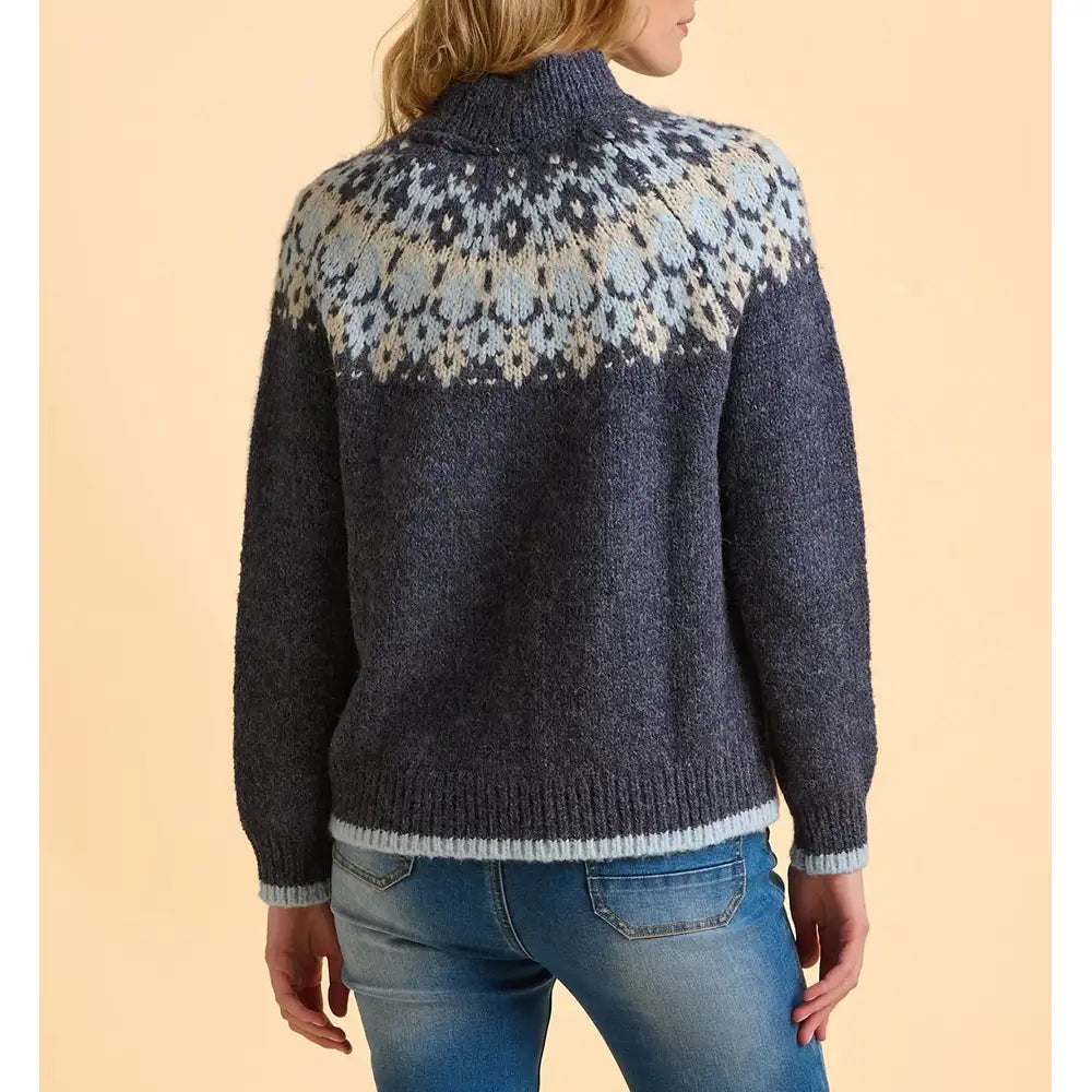 Person wearing a dark blue knitted sweater with a patterned yoke against a beige background