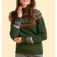 Person wearing a green knitted sweater with patterned sleeves against a beige background
