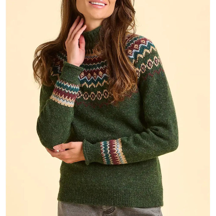 Person wearing a green knitted sweater with patterned sleeves against a beige background