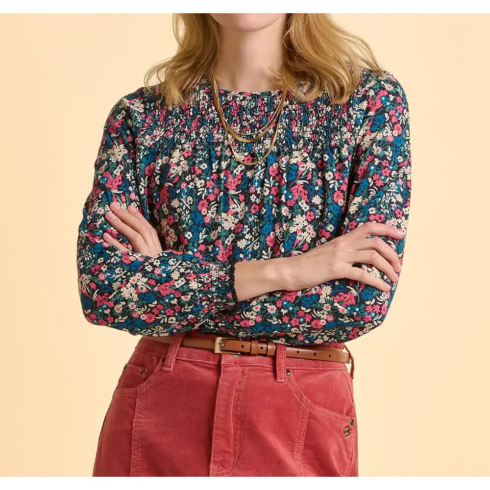 Person wearing a floral blouse and red pants on a beige background