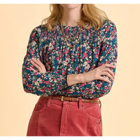 Person wearing a floral blouse and red pants on a beige background